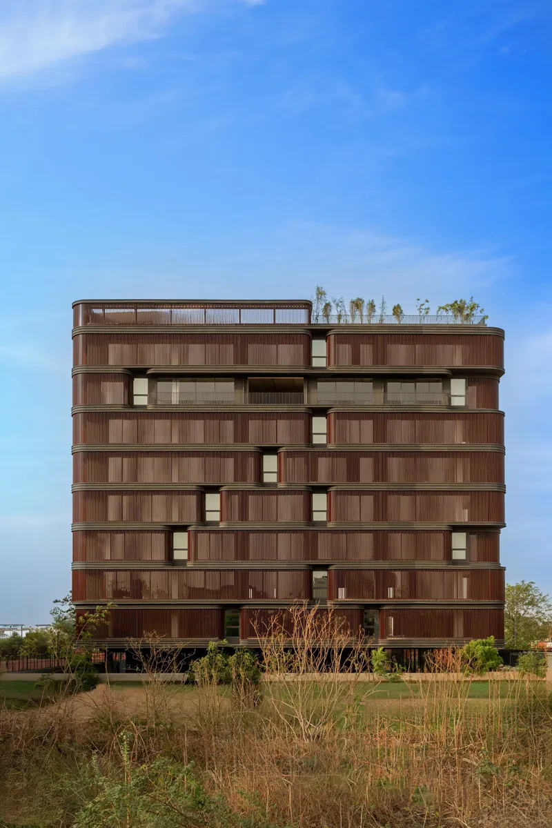 Rear elevation showing layered timber screens and rooftop plantings against dry grasses in foreground