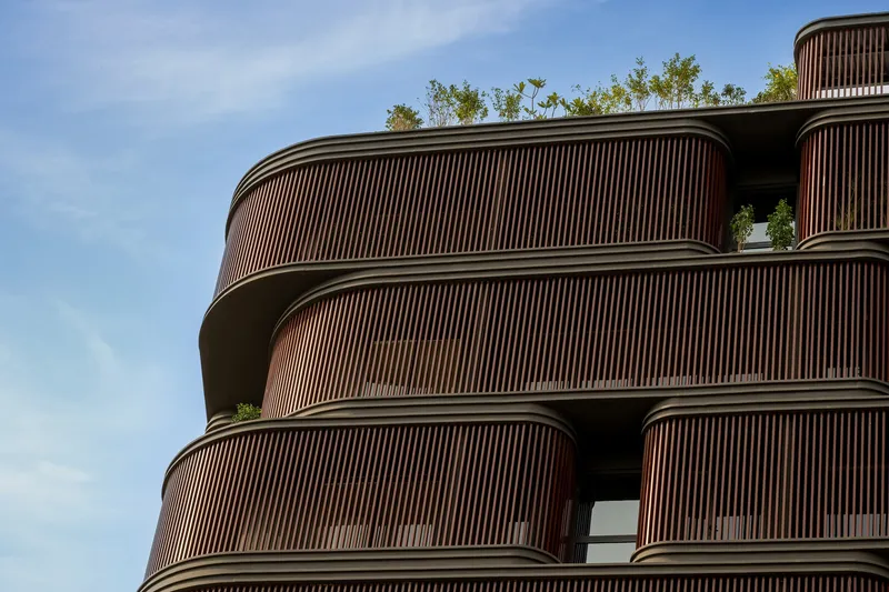 Stacked rounded balconies with vertical timber screens and plantings along the roofline
