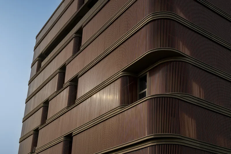 Facade detail of the timber louvered screens at dusk with recessed balcony openings