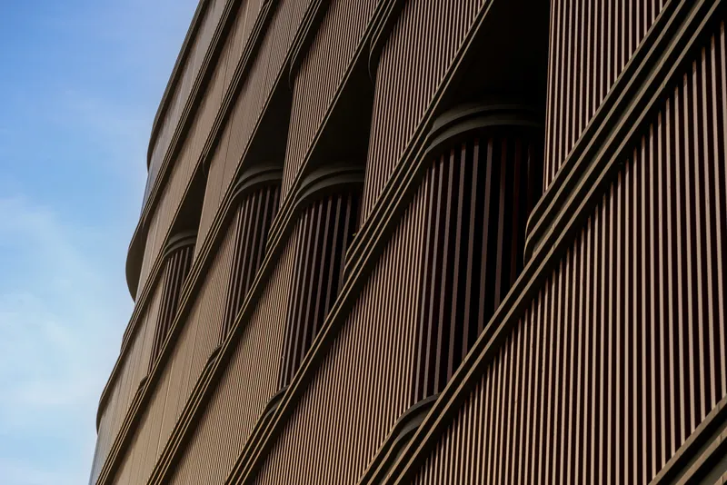 Close-up of the curved facade with vertical bronze-toned louvers creating arched openings against a blue sky