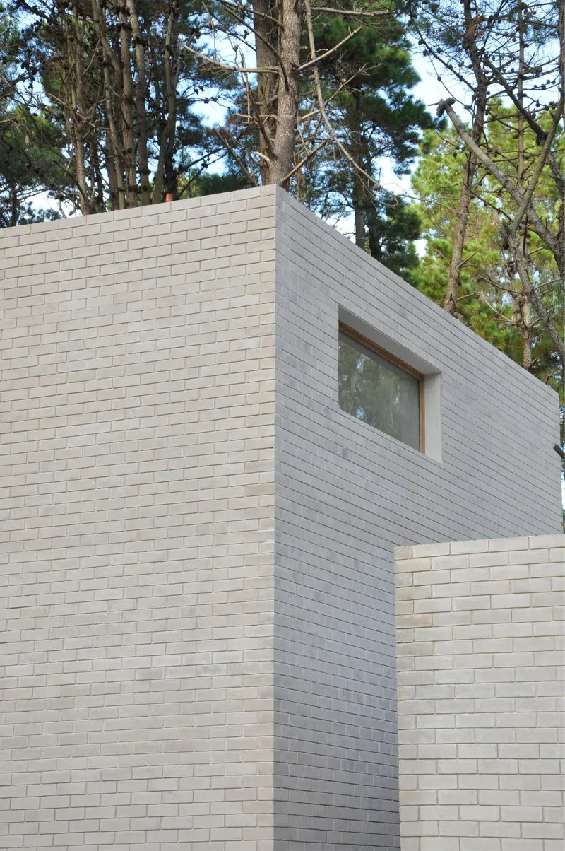 Angled white brick volumes meeting at corner with single timber window above