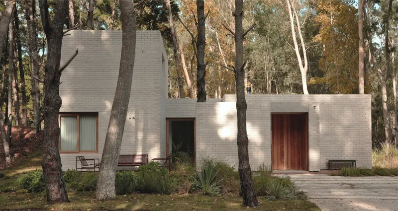 Street view of grey brick facade with timber door and openings among tall trees