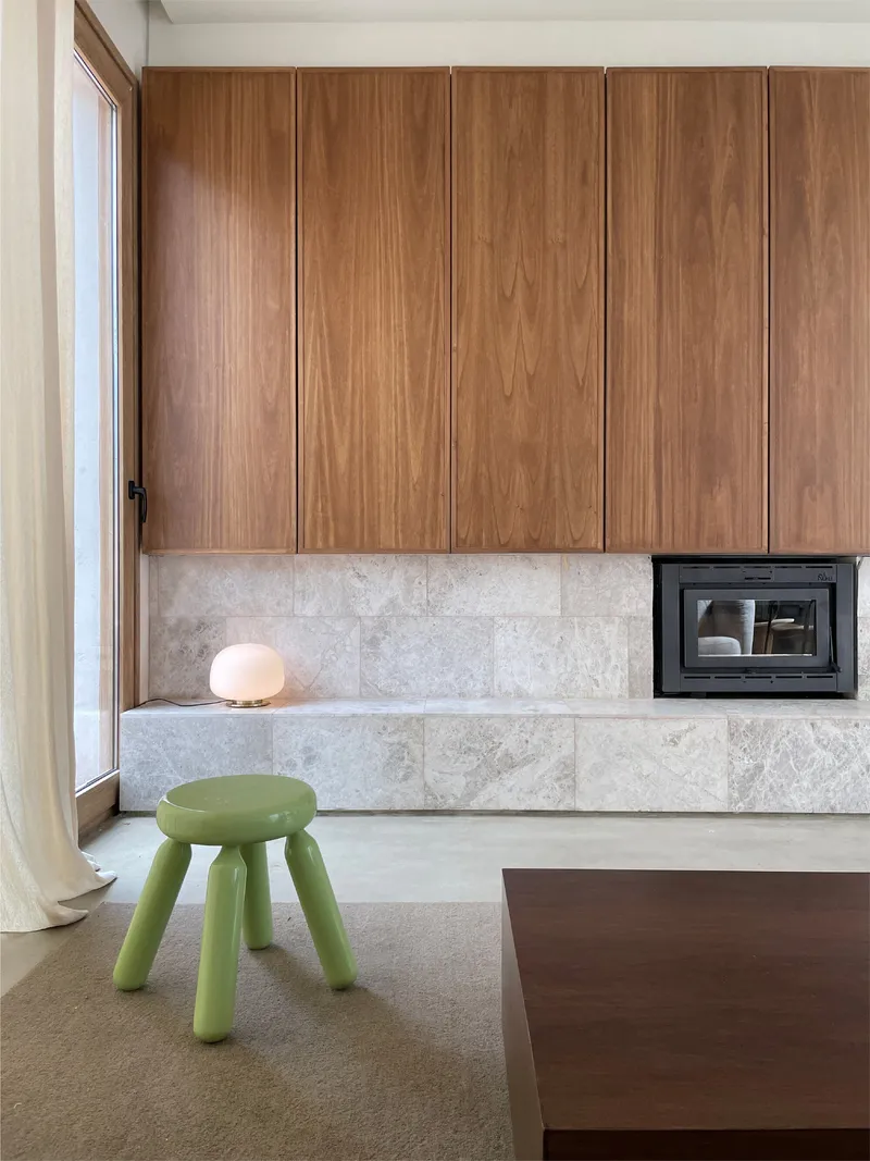Living room fireplace with wood cabinetry, stone surround, and green stool beside window