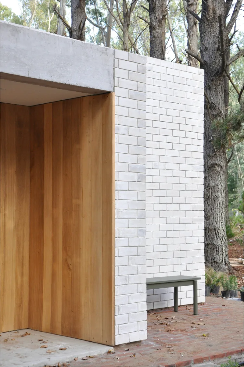 Exterior corner showing white brick wall, timber cladding and concrete lintel among trees
