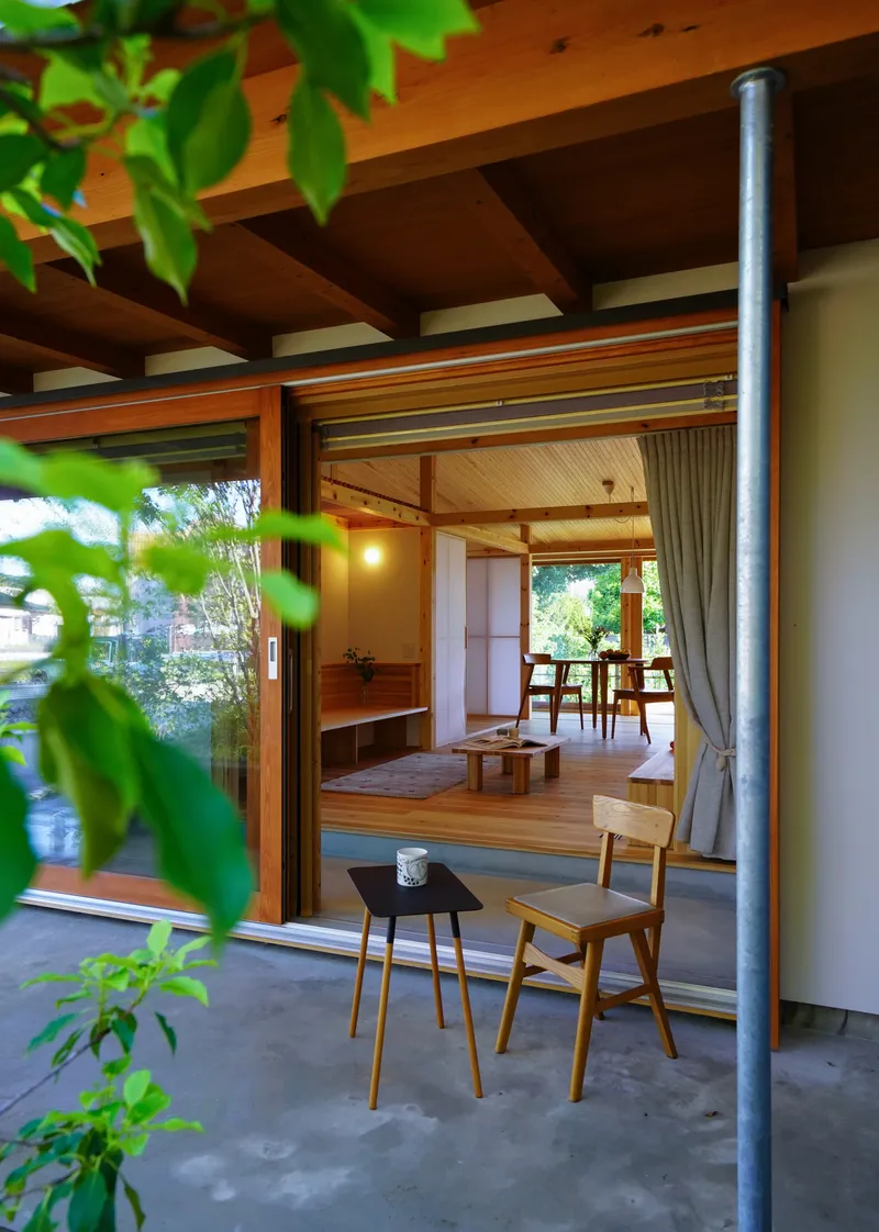 View from covered exterior terrace into living space with exposed timber beams and tree foliage framing