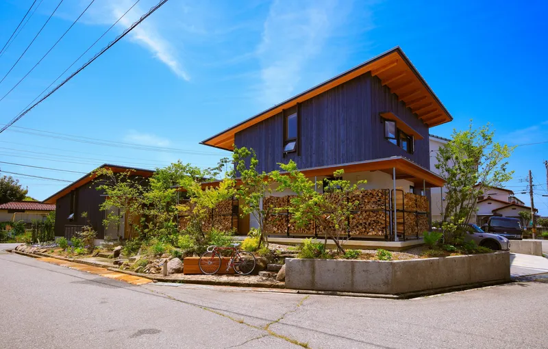 Street view of dark timber clad volumes with tilted roofs above a planted concrete curb