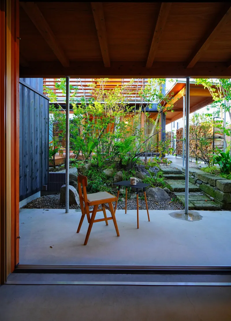 View from interior through sliding glass doors to courtyard garden with charred timber wall and horizontal screens