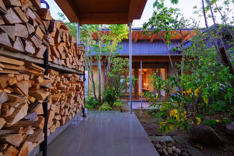 Stacked firewood wall beside concrete walkway leading to courtyard garden at dusk