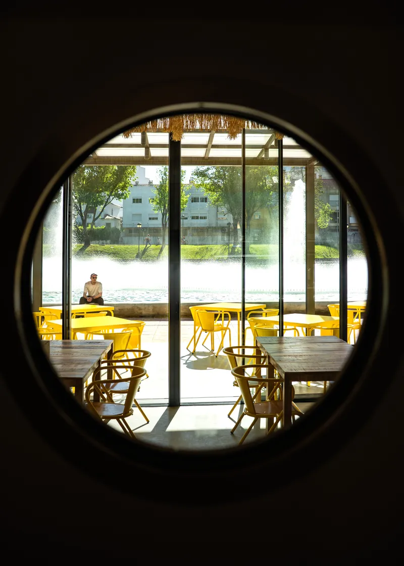 View through circular portal opening to dining area with yellow seating and glazed facade beyond