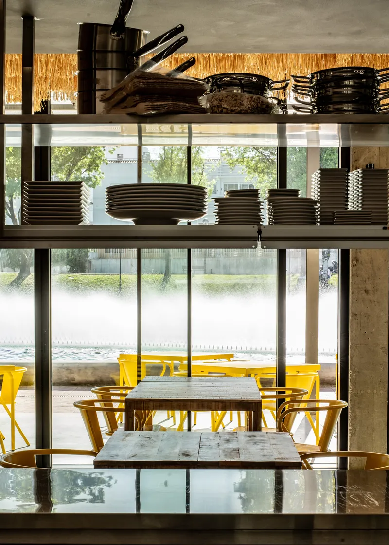 Open kitchen shelving with stacked plates and cookware framed by frosted glass windows overlooking the plaza