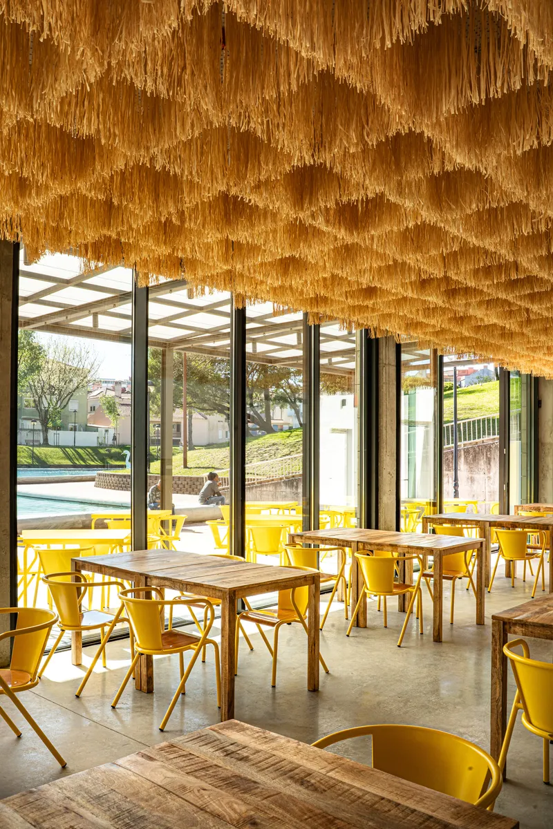 Dining area beneath a woven raffia ceiling canopy with views to the lawn through full-height windows