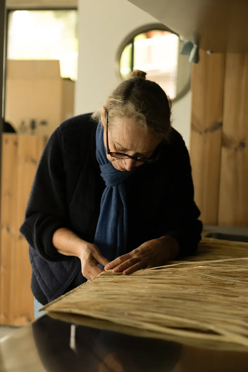 Craftsperson sanding a curved timber panel in a workshop with arched openings behind
