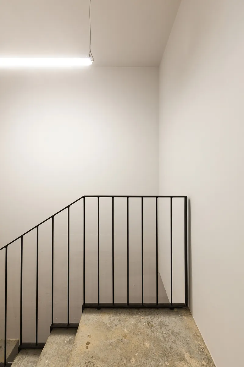 Stairwell with slender black metal railing ascending between white plaster walls under a skylight