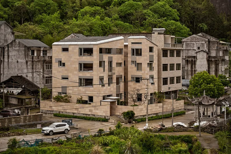 Aerial view of the rammed earth apartment block nestled among weathered village structures and lush hillside
