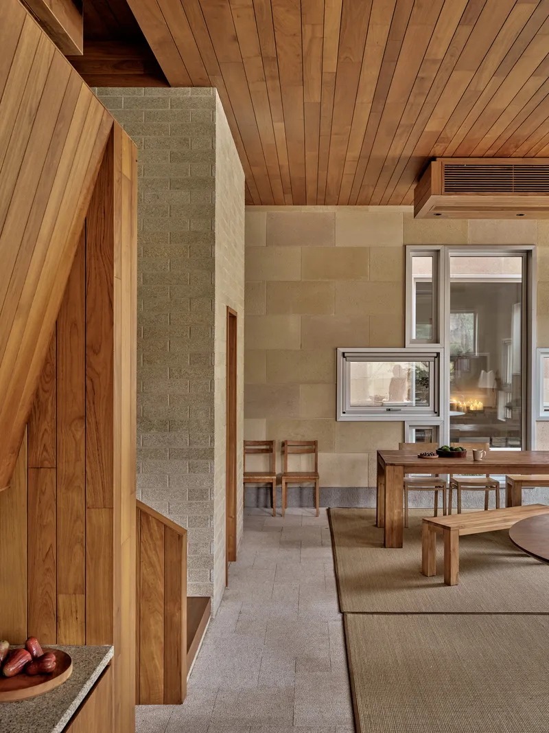 Living area with timber ceiling, concrete block walls and a double-sided fireplace connecting to the dining space