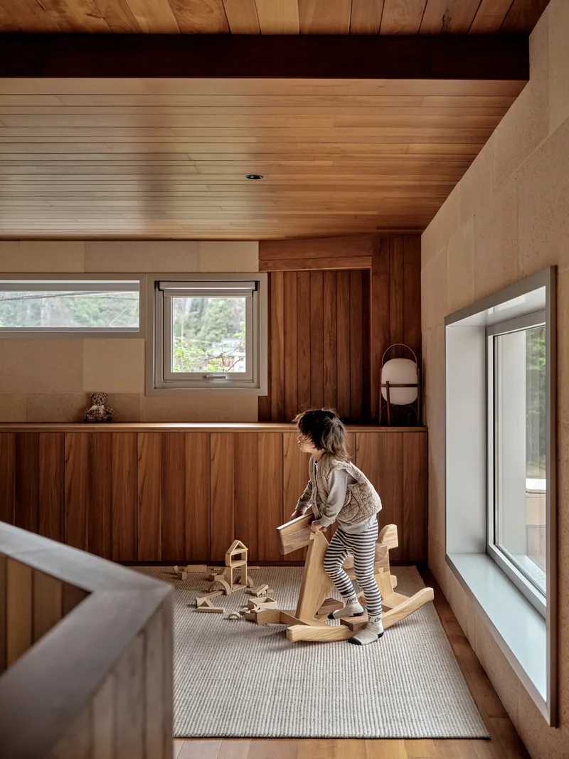 Interior play area with timber ceiling and cabinetry as a child arranges wooden blocks on a rug