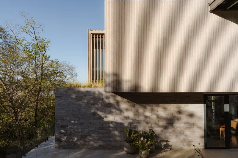 Exterior corner showing stacked stone base supporting vertical timber slat cladding with planted foreground