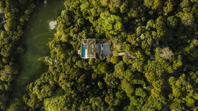 Aerial view of the residence with pool and flat roof nestled in dense forest canopy