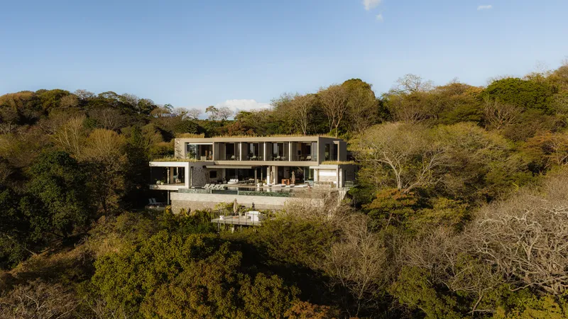 Two-story facade with horizontal bands of glazing and terrace embedded in tropical hillside vegetation