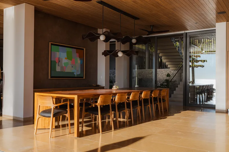 Dining area with timber table and pendant lights beneath wood slat ceiling looking toward exterior stairs
