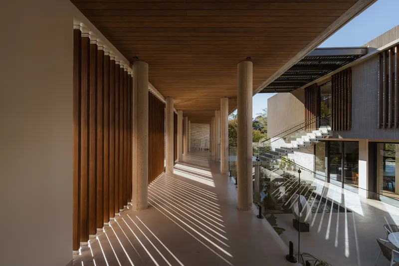 Covered walkway with concrete columns and timber ceiling casting striped shadows across the floor