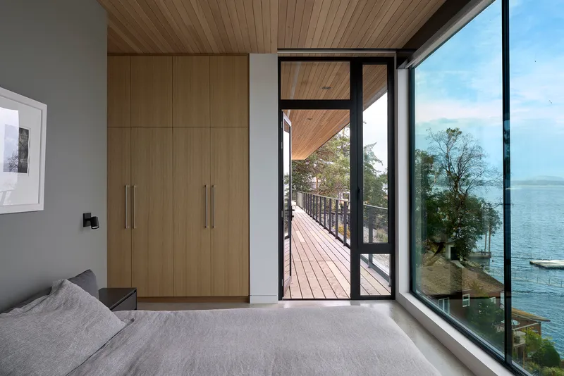 Bedroom with wood storage wall, glazed door opening to a timber deck with lake view