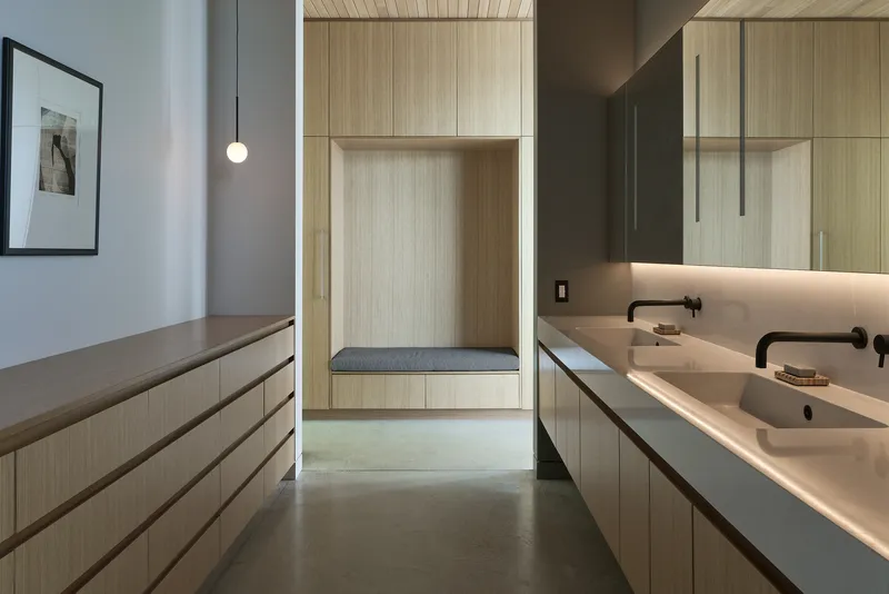 Bathroom vanity with light wood cabinetry and built-in seating nook illuminated by concealed strip lighting
