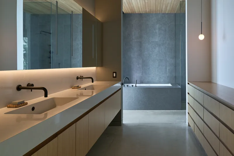Bathroom with concrete double vanity, black fixtures, and grey plaster walls under a timber ceiling
