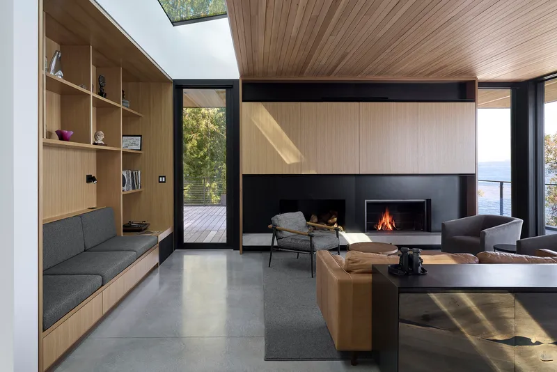 Living room with timber shelving wall, steel fireplace, and skylights casting afternoon light on concrete floors
