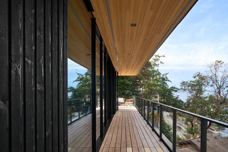 Timber deck walkway with steel railings alongside charred wood cladding under a clear blue sky