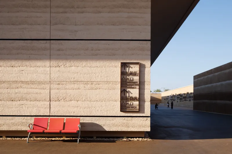 Travertine wall detail with recessed bronze panel above a red bench in sharp shadow