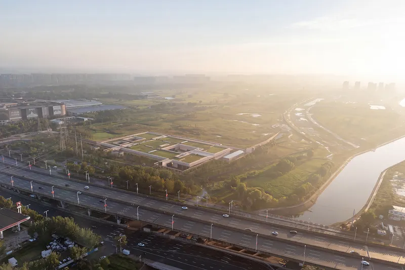 Aerial view of a walled compound with nested courtyards set in open grassland near a highway at sunrise