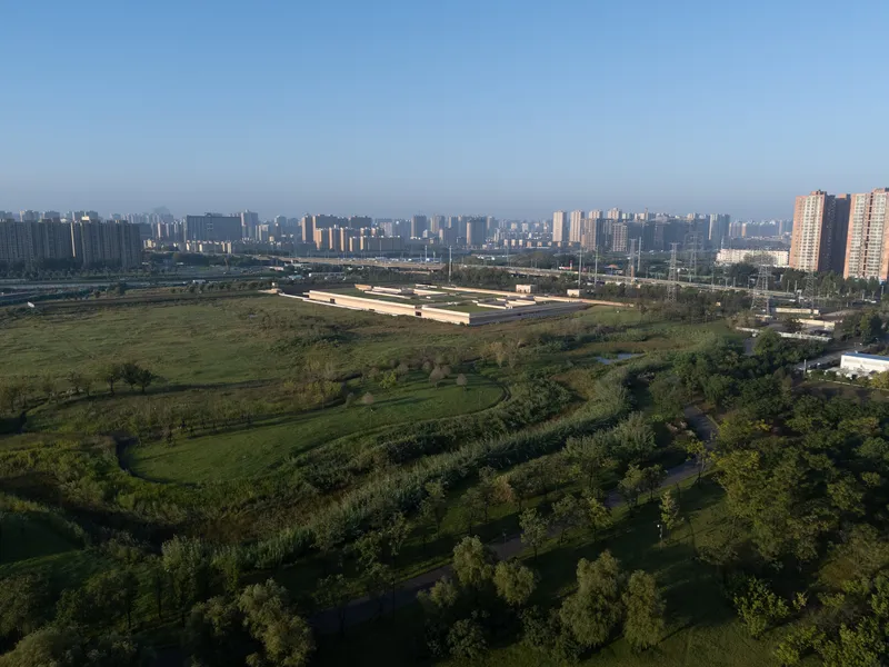 Distant view of the horizontal complex surrounded by planted berms and trees with residential towers beyond
