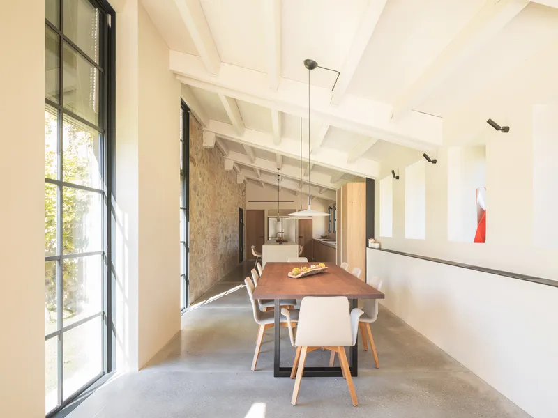 Dining area with tall steel-framed windows and exposed timber ceiling joists spanning the length