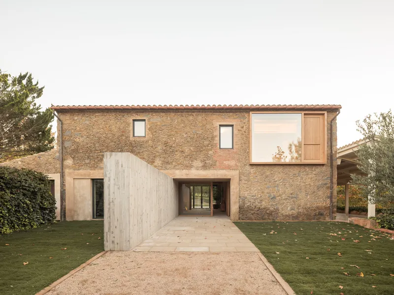 Stone facade with terracotta tile roof and timber-screened entryway under an overcast sky