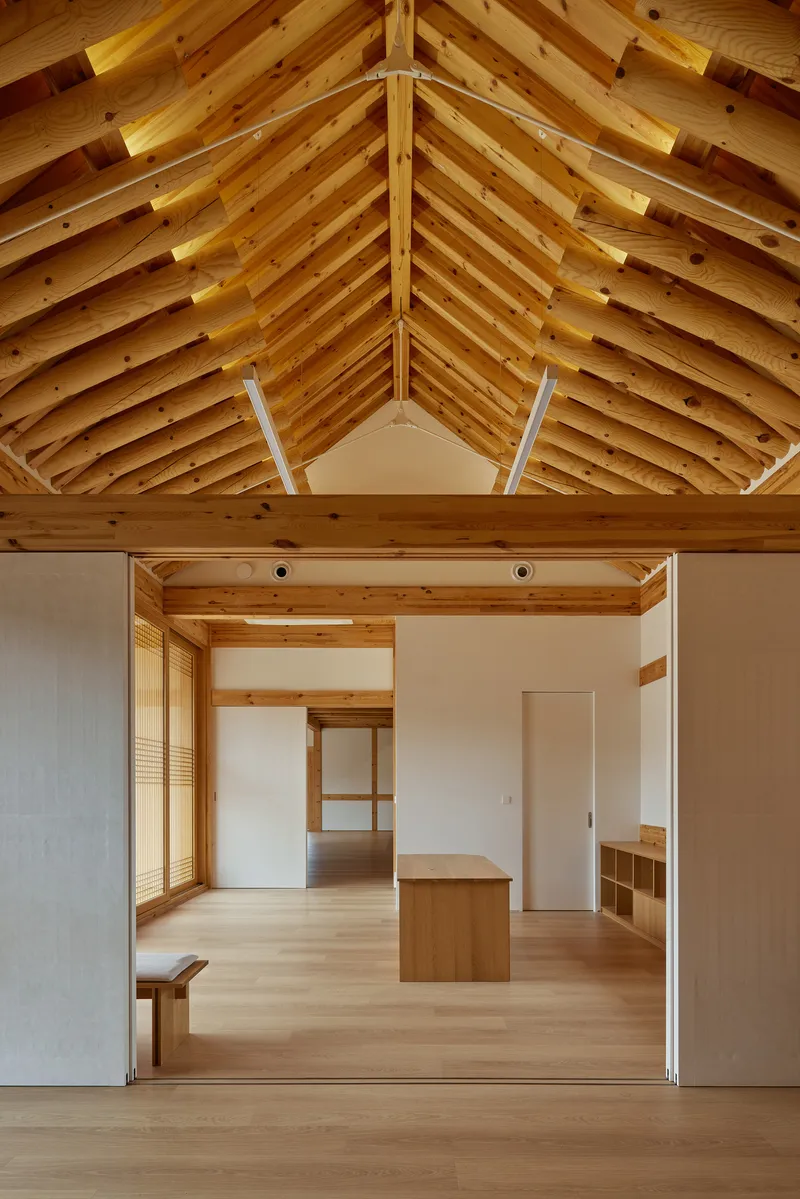 Open interior space with exposed timber rafters above and pale wood flooring extending through multiple rooms