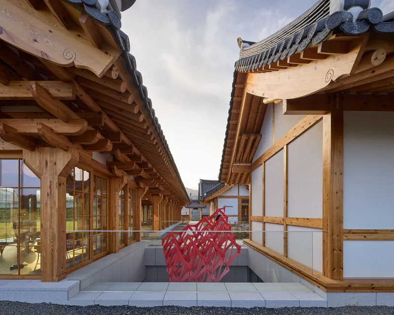 Sunken courtyard passage flanked by timber structures with a red sculptural installation at its center