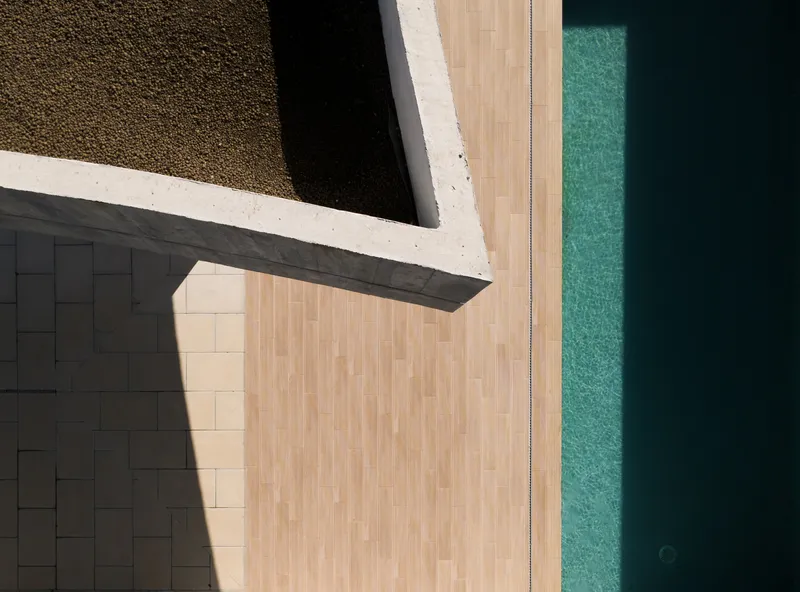 Overhead view of the concrete roof edge meeting timber decking and a turquoise pool in bright sunlight