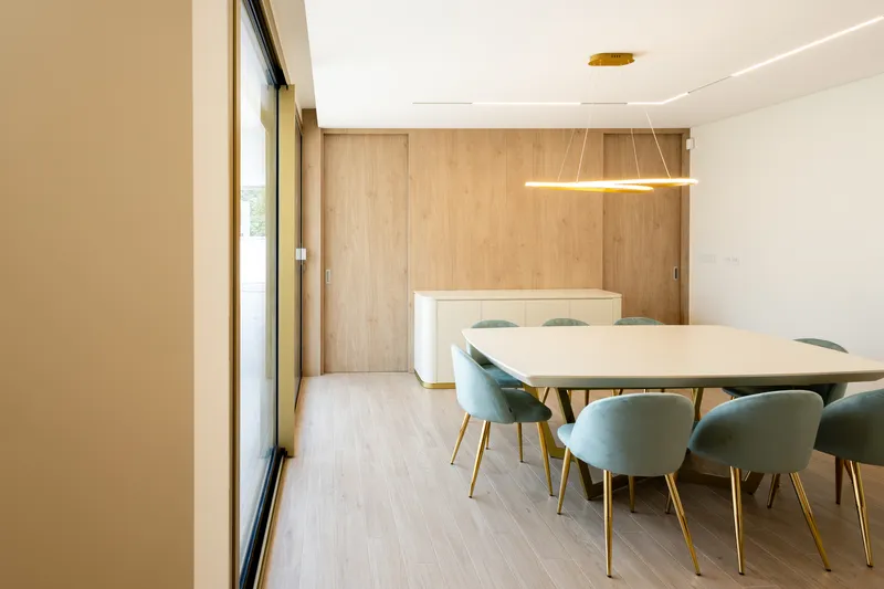 Dining area with suspended linear pendant over white table and timber sliding wall panels in daylight