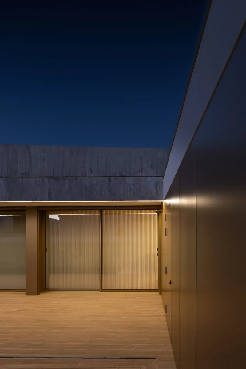 Covered timber deck with sliding glass doors and vertical wood-slat screens at twilight