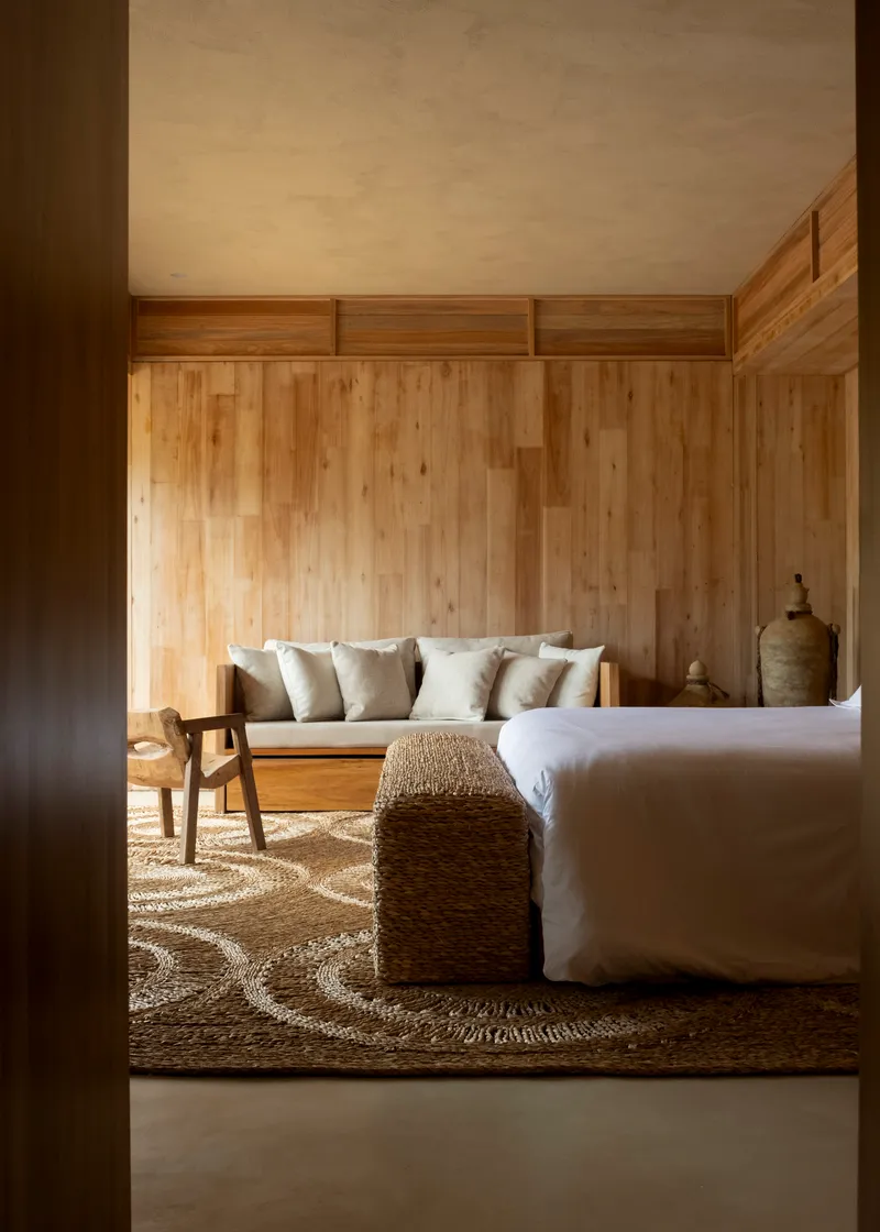 Bedroom interior with vertical timber plank walls and transom windows filtering afternoon light across a jute rug