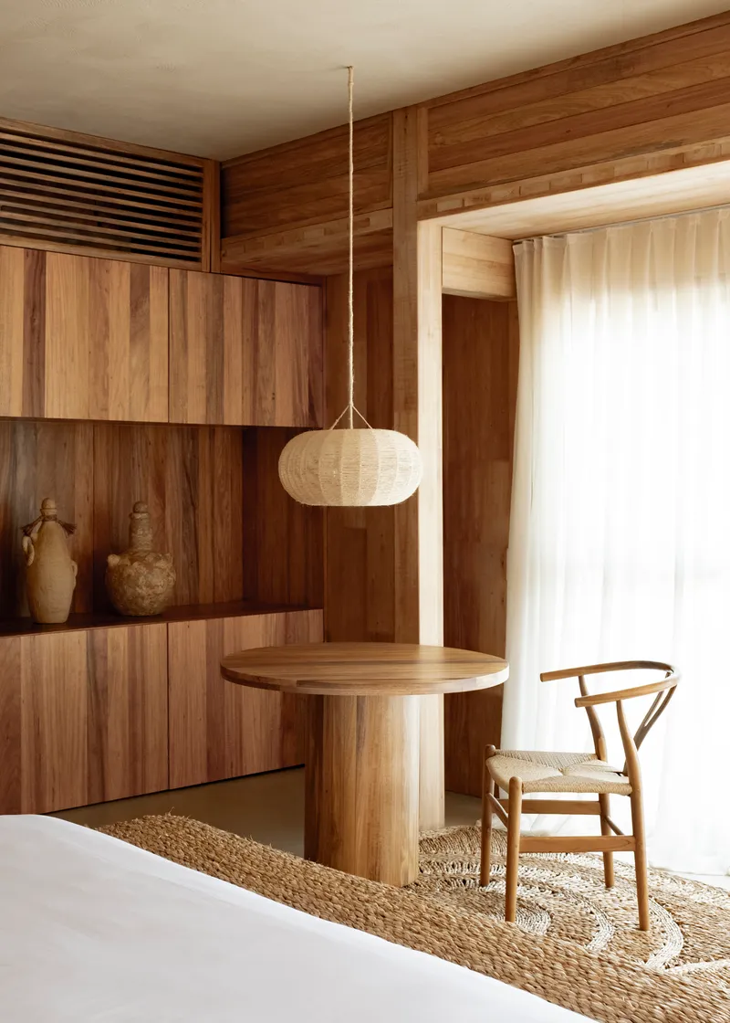 Interior corner with timber-paneled walls, built-in shelving, pendant lamp, and woven rug below a white curtain