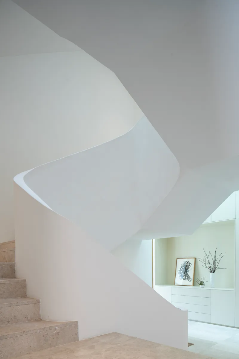 Sculptural white plaster staircase with spiraling wall and travertine treads under soft daylight
