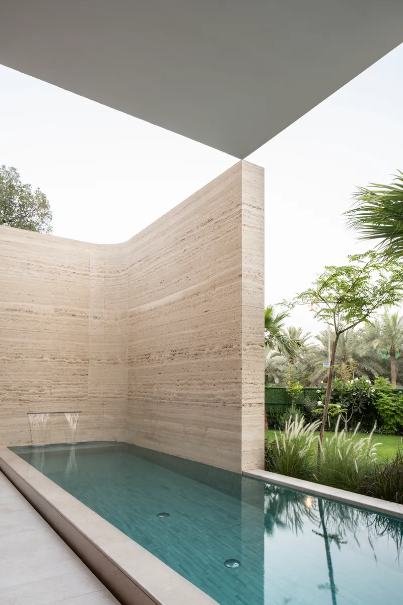 Corner courtyard pool enclosed by horizontal banded travertine walls beneath an angled white overhang