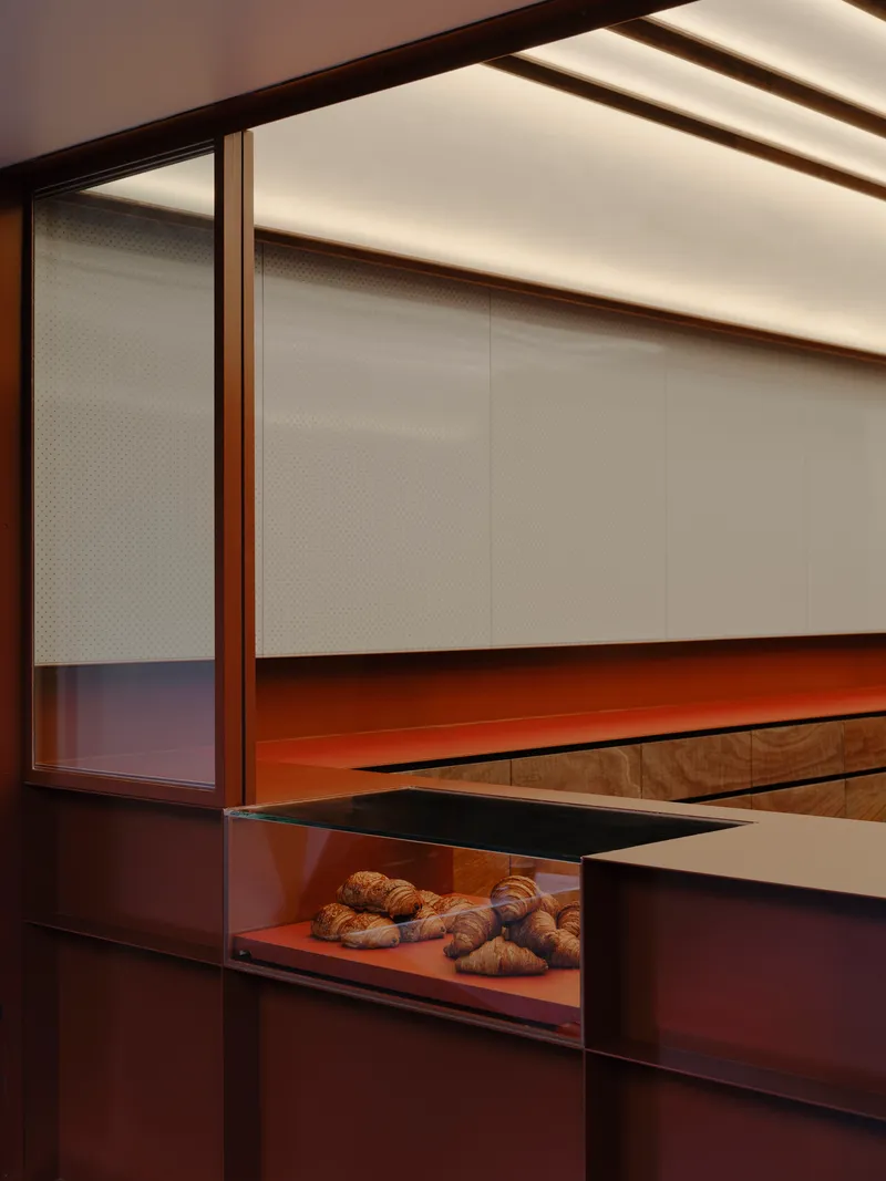 Close-up of the translucent perforated panels and red metal counter with pastries displayed below