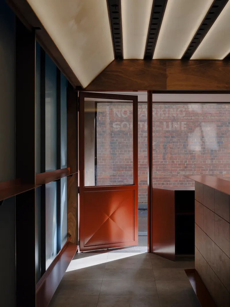 View toward the red metal door opening onto the brick courtyard under the timber canopy