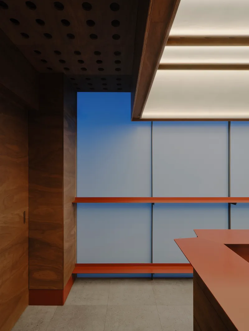 Corner view showing perforated ceiling panel, timber cabinetry and the layered glass and copper elements