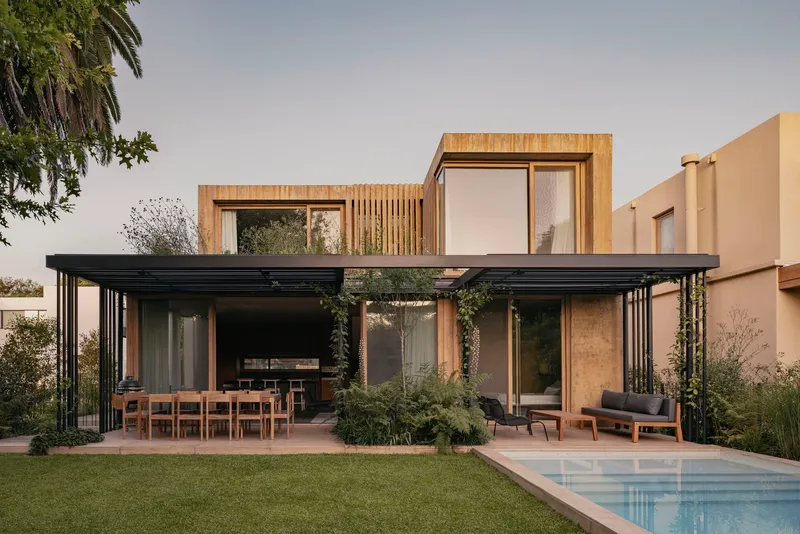 Garden elevation showing black steel pergola sheltering outdoor dining area beside pool and lawn