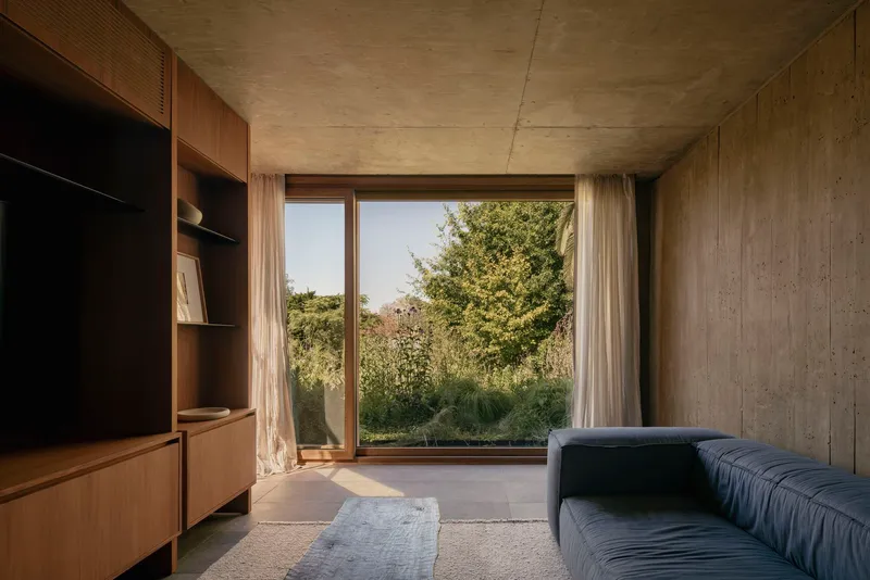 Living room with board-marked concrete walls and timber joinery framing glazed corner window