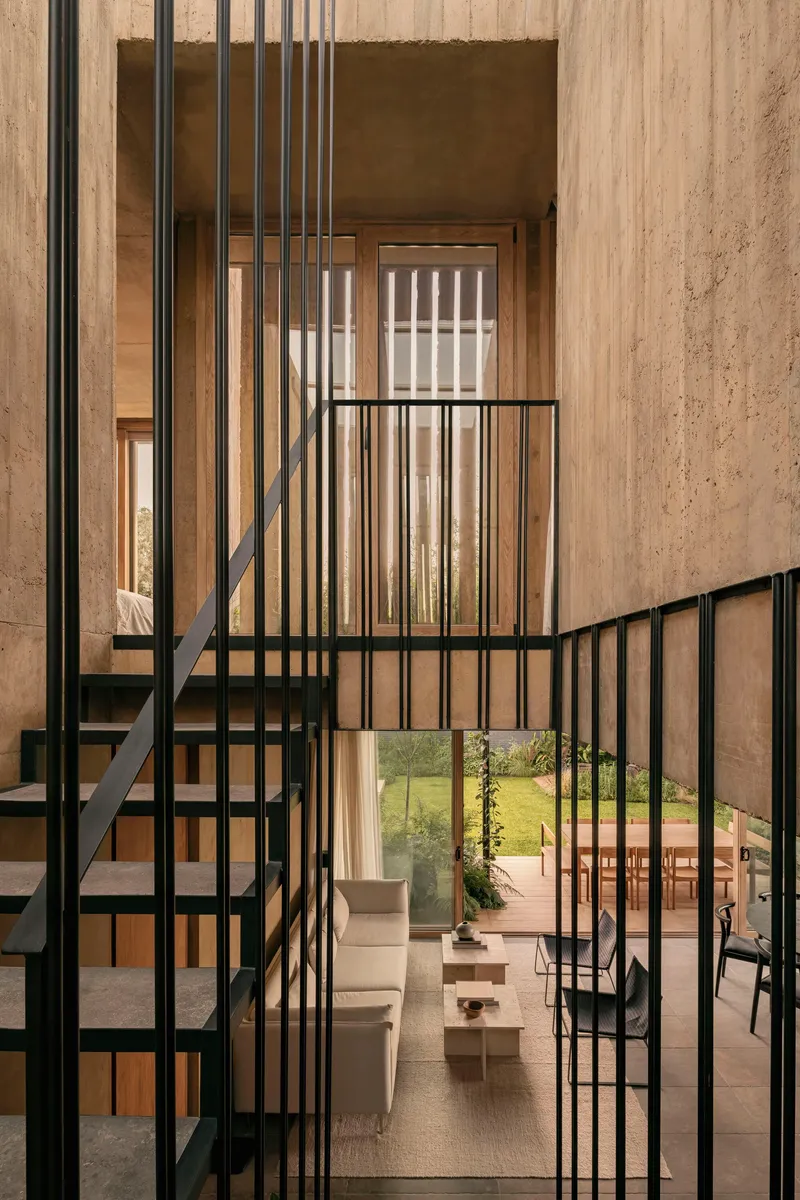 Double-height void with black metal staircase and vertical slat screen against board-formed concrete walls